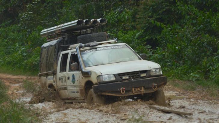 Un pick-up, transportant des tôles enroulées, embourbé sur une piste de fortune